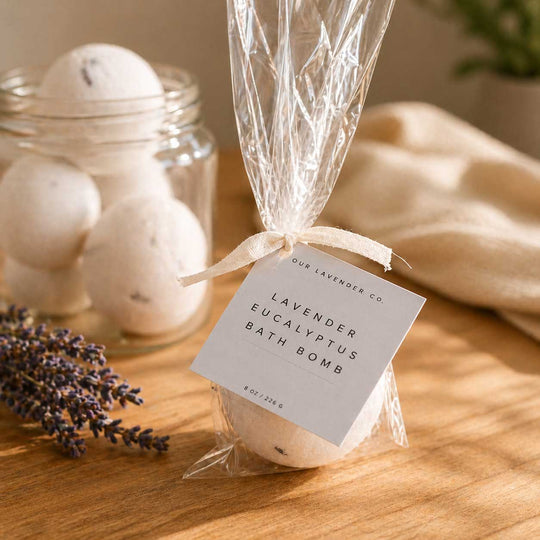 Lavender and eucalyptus bath bomb in a clear bag with a label, jar of bath bombs, and lavender flowers on a wooden surface.