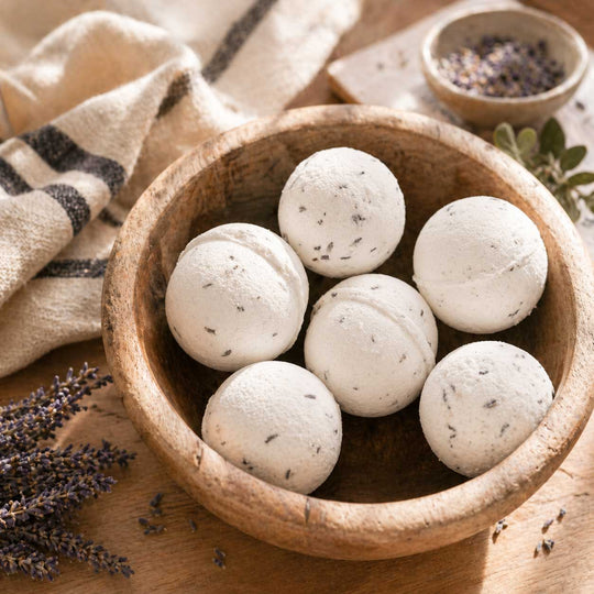 Wooden bowl filled with white bath bombs with specks on a wooden surface with lavender.