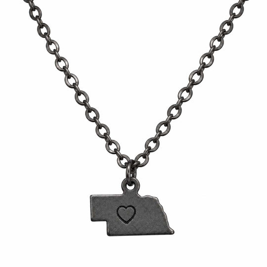 A dark gunmetal gray necklace featuring a pendant shaped like the state of Nebraska, with a small heart cutout in the center, displayed against a solid white background.