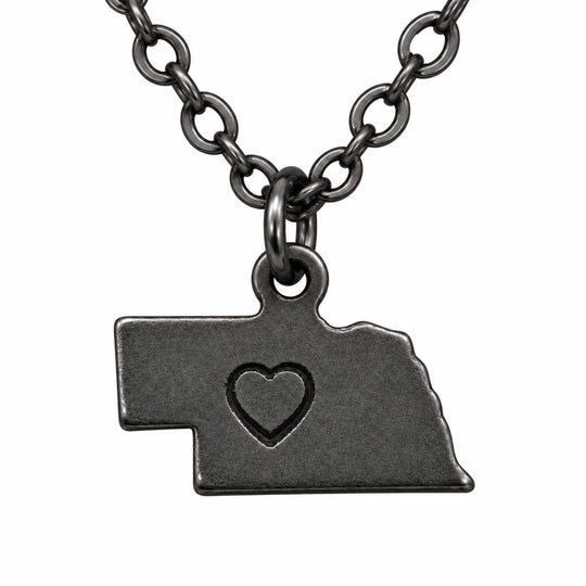 A dark gunmetal gray necklace featuring a pendant shaped like the state of Nebraska, with a small heart cutout in the center, displayed against a solid white background.