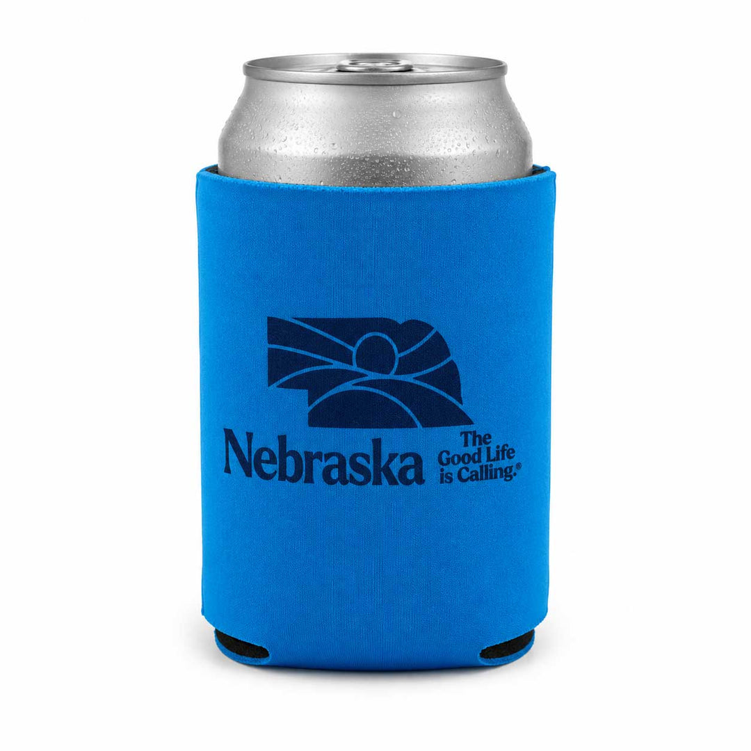 A bright blue neoprene can cooler sleeve with a dark blue Nebraska state graphic and the text 'Nebraska The Good Life is Calling' on a white background, holding a silver aluminum can.