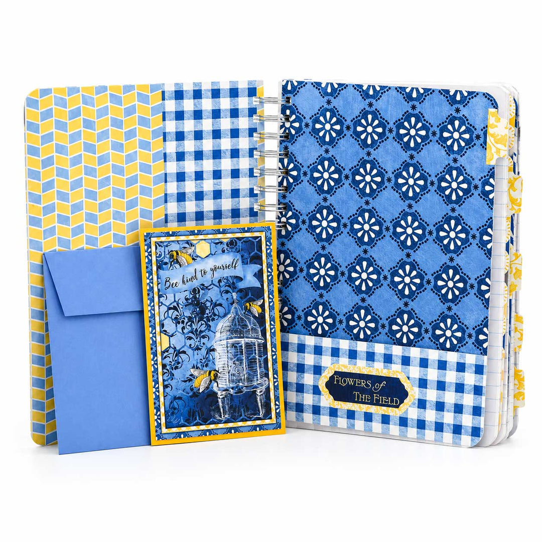 A decorative gift set featuring a blue and yellow patterned notebook or journal, a matching blue envelope, and a small card with a birdcage illustration and the words 'So be it with yourself.' The set is photographed on a clean white background.