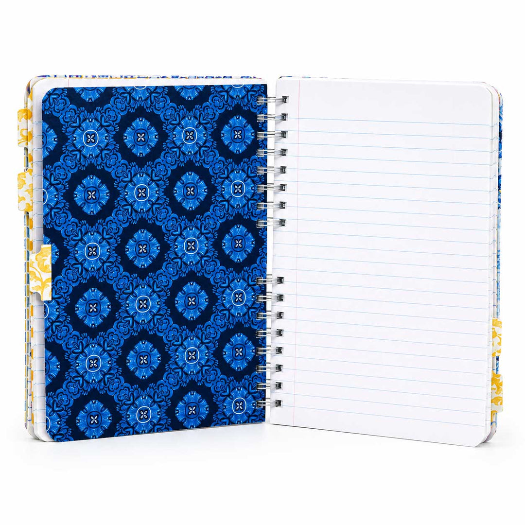 An open spiral-bound notebook with a blue patterned cover on the left and lined blank pages on the right, shown on a white background.