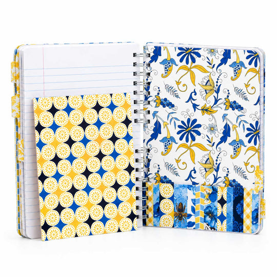 An open spiral-bound notebook with a decorative cover featuring blue, yellow, and white floral and geometric patterns, shown on a clean white background.