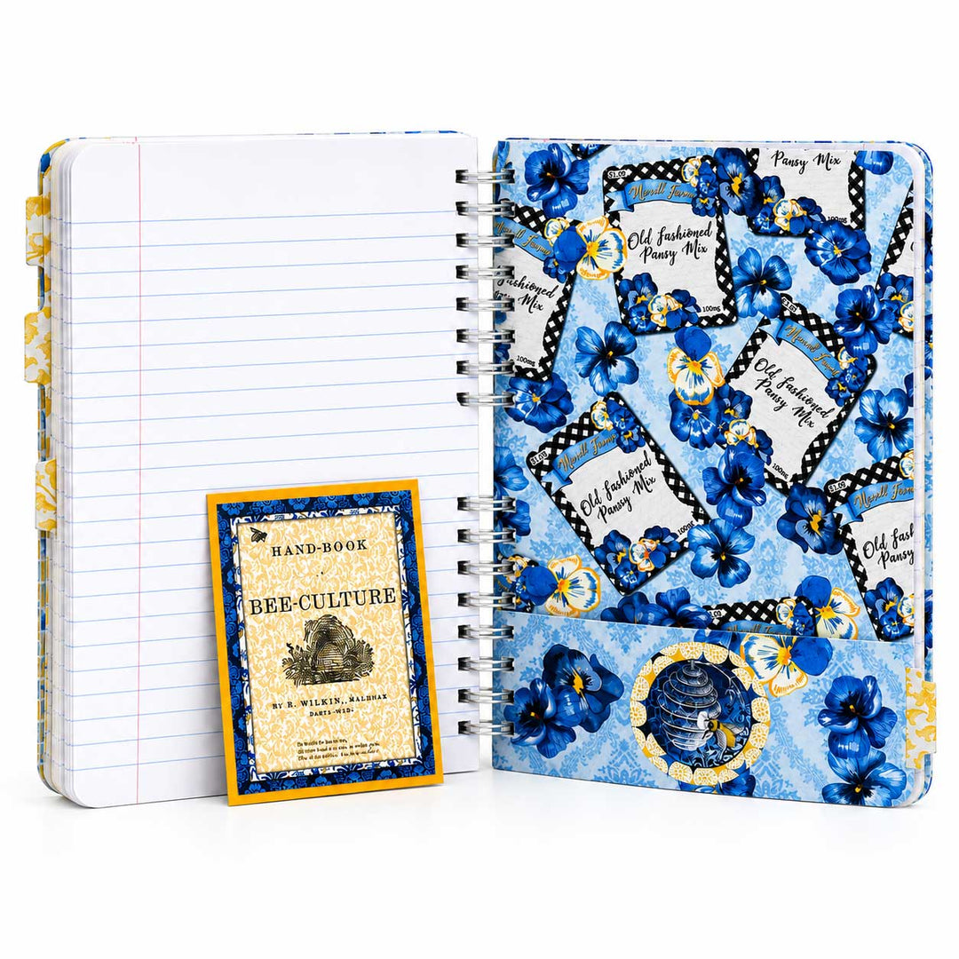 A spiral-bound notebook set shown open on a white background, featuring a blue floral patterned cover with pocket-style pages and a small booklet titled 'Handbook of Bee Culture' leaning against the left page.