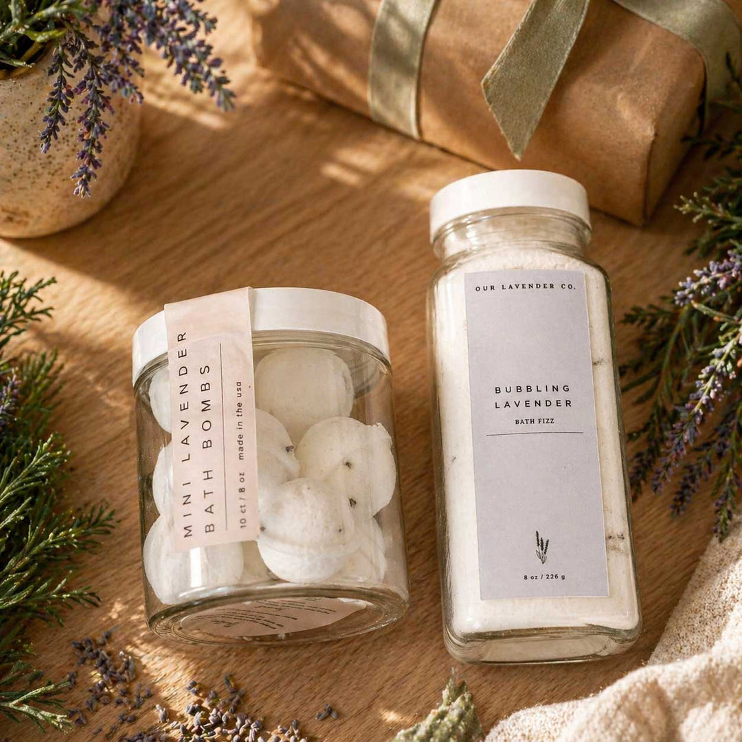 Two jars of bath products on a wooden surface with lavender and greenery.