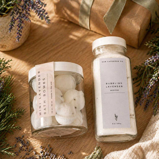 Two jars of bath products on a wooden surface with lavender and greenery.