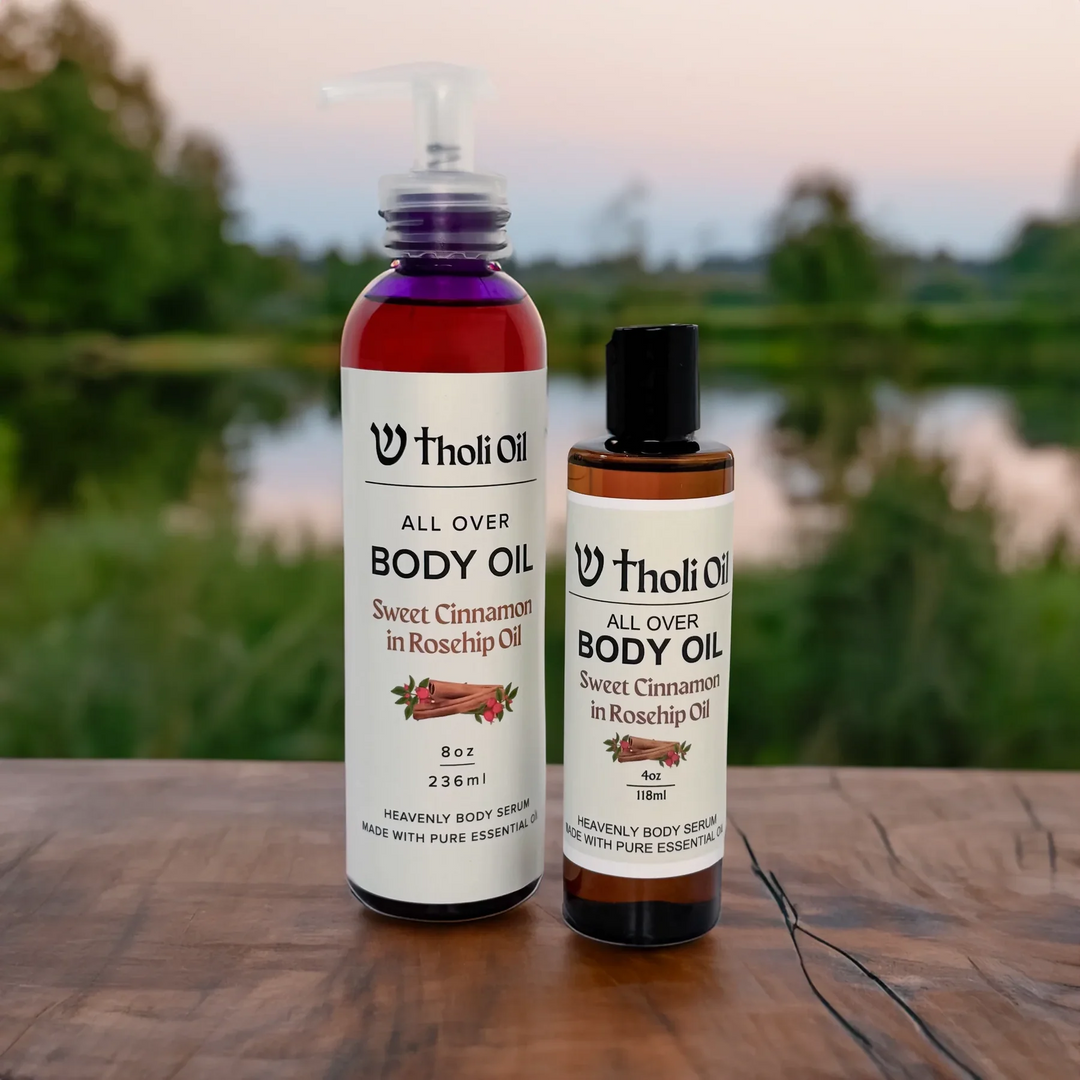 Two bottles of Tholi Oil body oil on a wooden surface with a blurred natural background