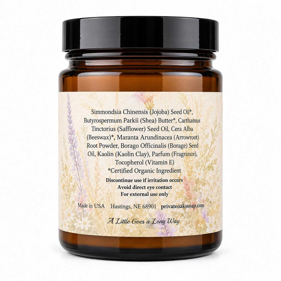 An amber glass jar with a black lid and a cream-colored label, photographed against a clean white background. The label features botanical illustrations and lists Simondesia Chinensis (Jojoba) Seed Oil as the primary product ingredient, along with other natural ingredients like Shea Butter and Carthamus Tinctorius.