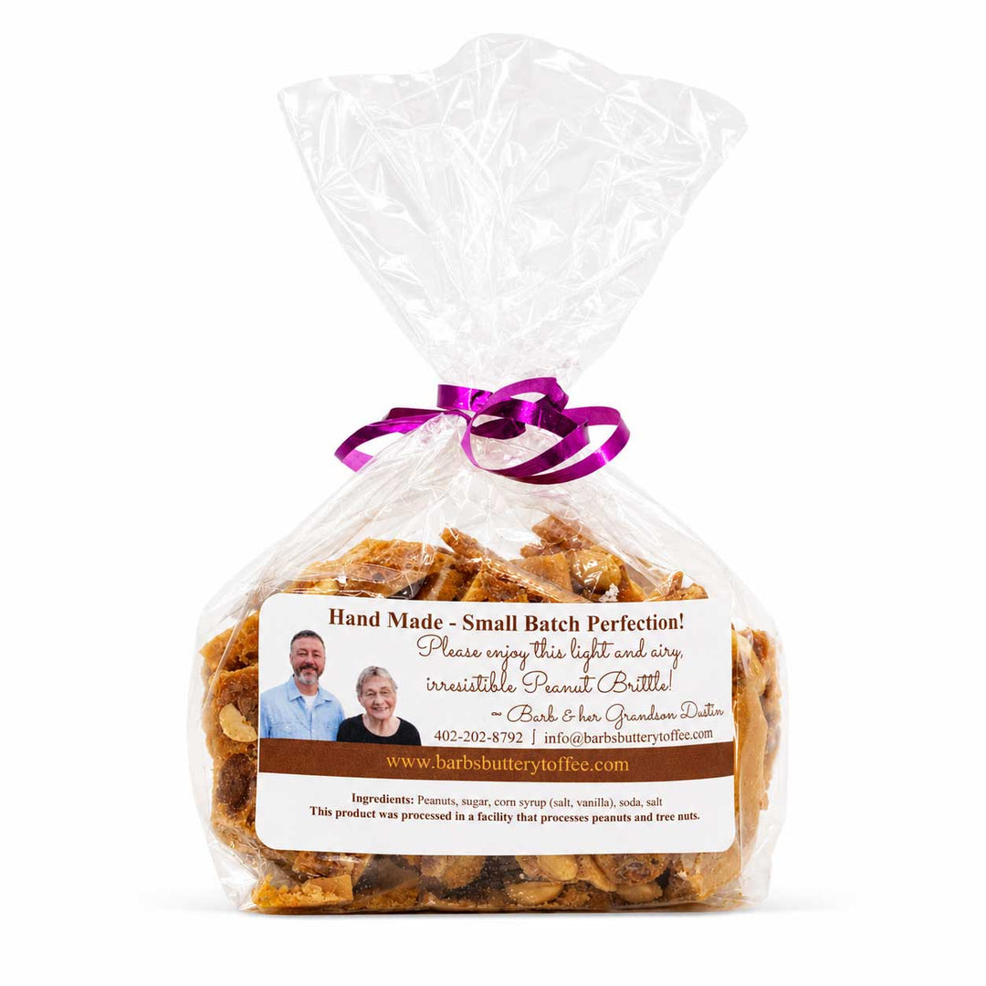 A clear plastic bag filled with small brown peanut butter candies, tied with a purple ribbon, and featuring a white and brown label with a family photo and the brand name Barb & Ken's Quaker Oats.