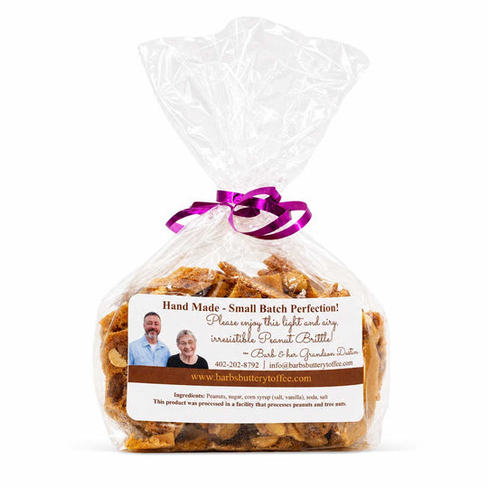 A clear plastic bag filled with small brown peanut butter candies, tied with a purple ribbon, and featuring a white and brown label with a family photo and the brand name Barb & Ken's Quaker Oats.