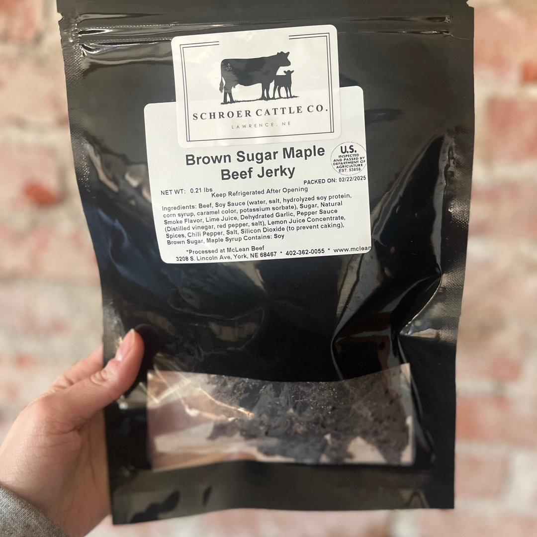 Black bag of Brown Sugar Maple Beef Jerky with Schrider Cattle Co. label held by a hand against a brick wall.