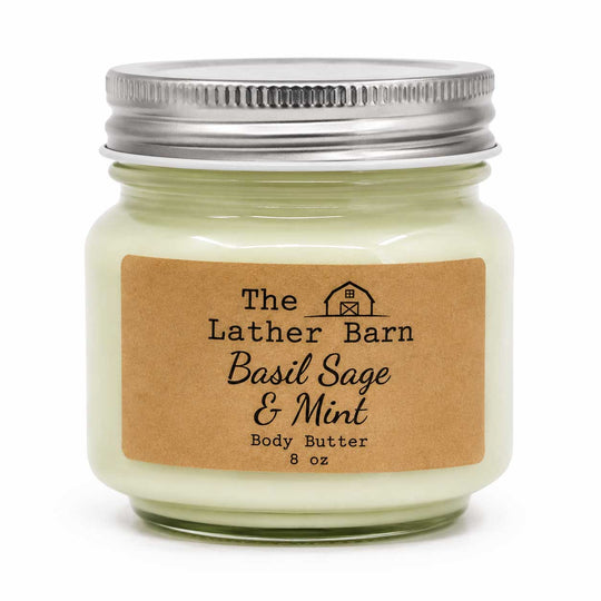 A 8 oz glass jar candle with a silver metal lid and a brown kraft paper label reading 'The Lather Barn Basil Sage & Mint Body Butter'.