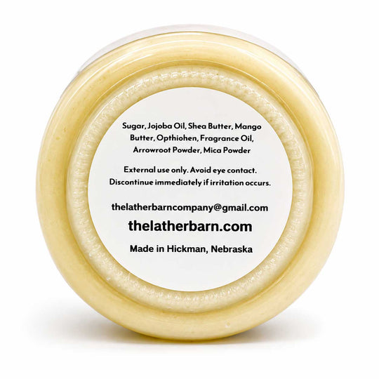 Top-down view of a round beige jar with a white label, showing product ingredients and the brand name 'The Leather Barn Company' on a white background.