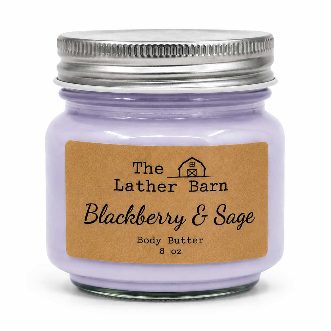 A 8 oz glass jar candle with light purple wax, a silver metal lid, and a brown kraft paper label reading 'The Lather Barn Blackberry & Sage Body Butter'.