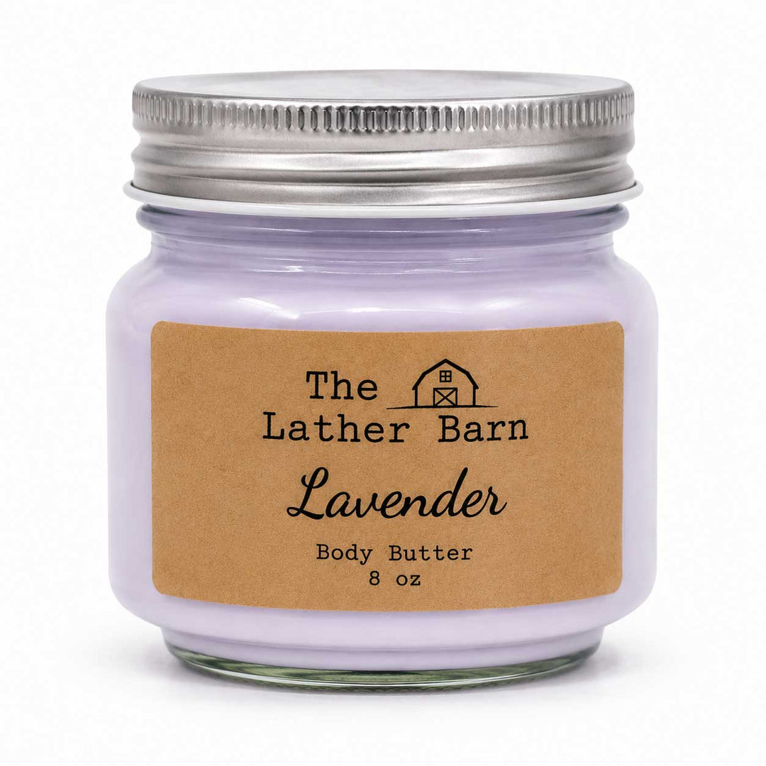 A lavender body butter candle in an 8 oz glass jar with a silver metal lid and a brown kraft paper label reading 'The Lather Barn Lavender Body Butter 8 oz'.