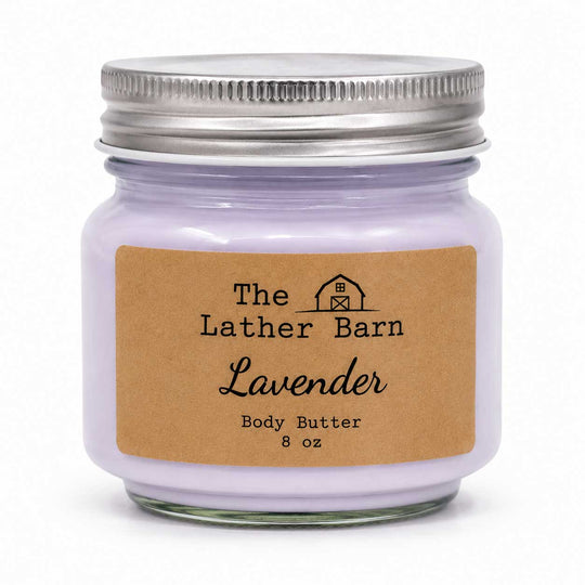 A lavender body butter candle in an 8 oz glass jar with a silver metal lid and a brown kraft paper label reading 'The Lather Barn Lavender Body Butter 8 oz'.