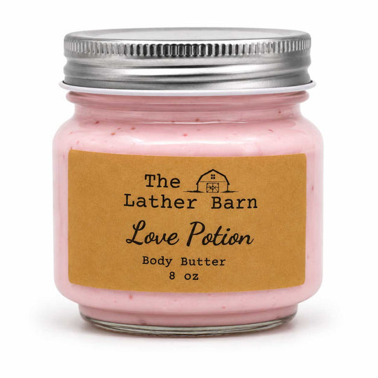 A 8 oz glass jar of 'Love Potion' body butter by The Lather Barn, filled with pink cream and sealed with a silver metal lid, set against a plain white background.