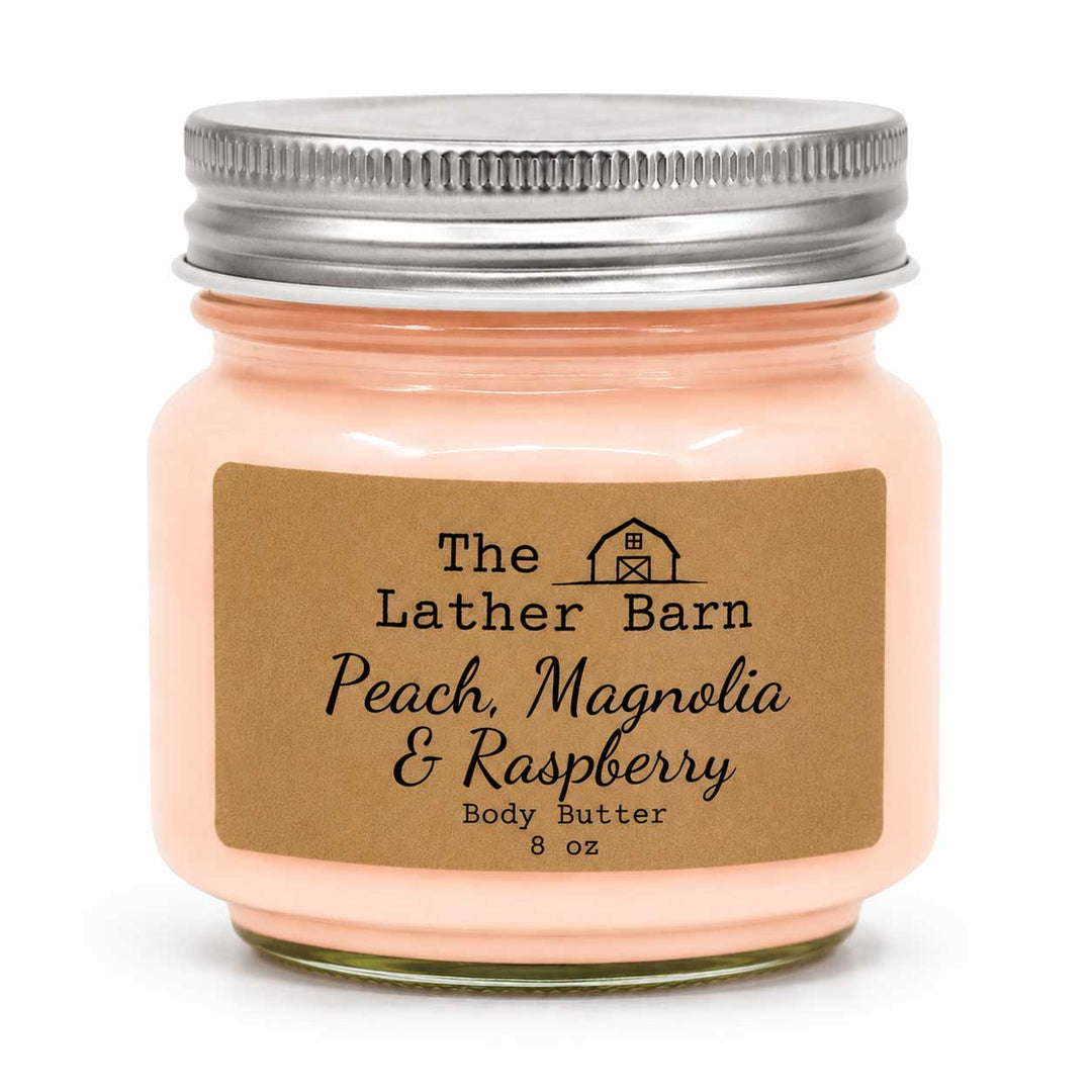 A 8 oz jar of peach-colored body butter with a brown kraft paper label reading 'The Lather Barn Peach, Magnolia & Raspberry Body Butter'. The jar has a silver metal screw lid and is set against a plain white background.