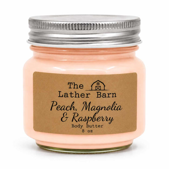 A 8 oz jar of peach-colored body butter with a brown kraft paper label reading 'The Lather Barn Peach, Magnolia & Raspberry Body Butter'. The jar has a silver metal screw lid and is set against a plain white background.