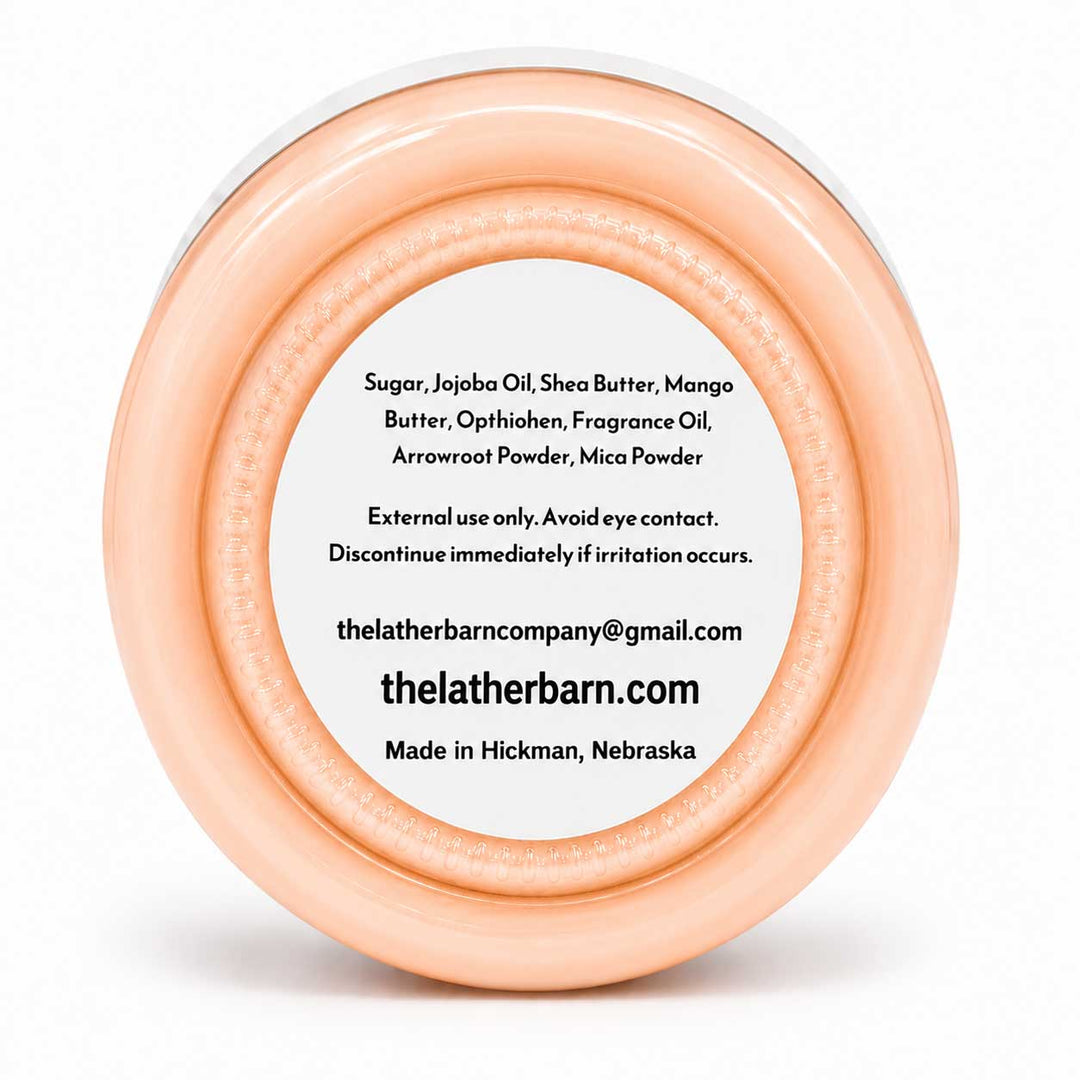 A round peach-colored cosmetic jar with a white lid, featuring a white label with black text listing ingredients and the brand name 'thelatherbarn.com'.