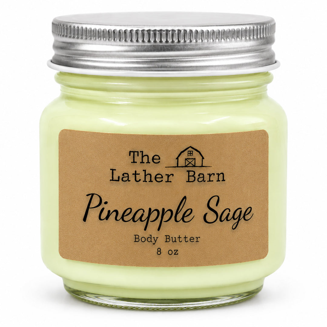 An 8 oz glass jar of body butter with pale yellow-green wax, a silver metal lid, and a brown kraft paper label reading 'The Lather Barn Pineapple Sage Body Butter 8 oz'.