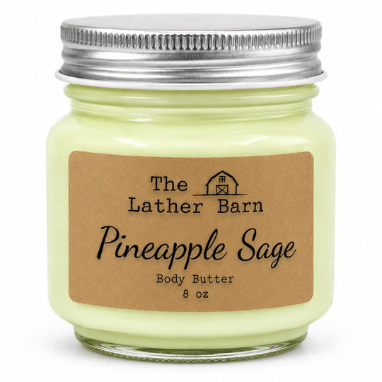 An 8 oz glass jar of body butter with pale yellow-green wax, a silver metal lid, and a brown kraft paper label reading 'The Lather Barn Pineapple Sage Body Butter 8 oz'.