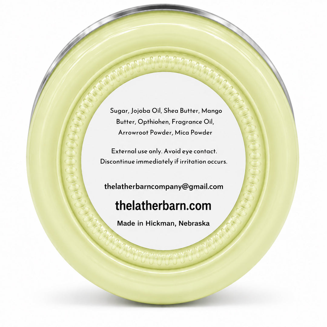 Top-down view of a round pale yellow cosmetic jar with a clear lid and a white label showing product ingredients and the brand thelatherbarn.com.