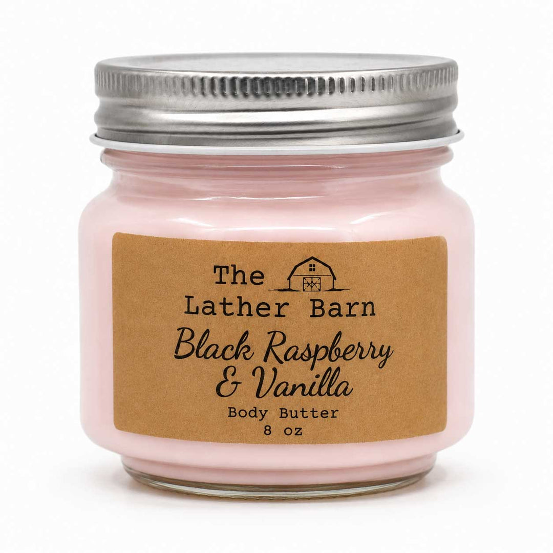 A 8 oz glass jar candle with a silver metal lid and a brown kraft paper label reading 'The Lather Barn Black Raspberry & Vanilla Body Butter'.
