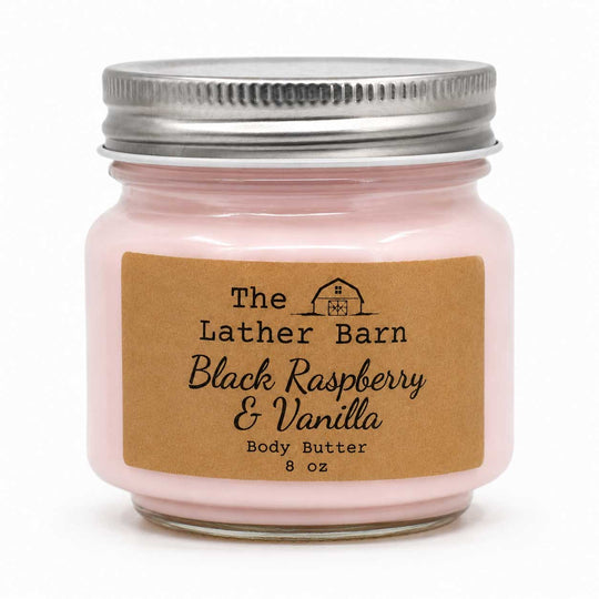 A 8 oz glass jar candle with a silver metal lid and a brown kraft paper label reading 'The Lather Barn Black Raspberry & Vanilla Body Butter'.