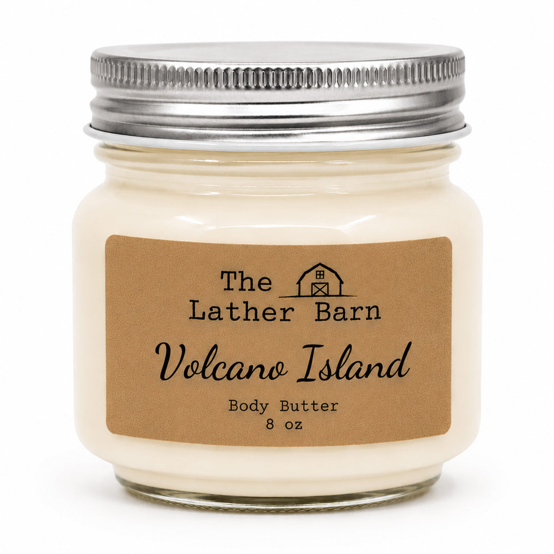 An 8 oz jar candle of body butter by The Lather Barn, featuring creamy off-white wax in a clear glass jar with a silver metal lid and a brown kraft paper label.