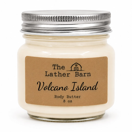 An 8 oz jar candle of body butter by The Lather Barn, featuring creamy off-white wax in a clear glass jar with a silver metal lid and a brown kraft paper label.