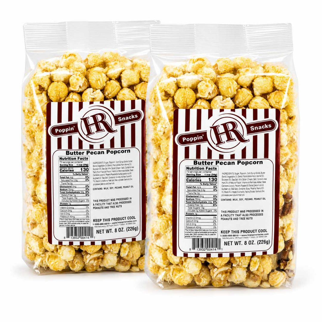 Two clear plastic bags of Poppin' HR Butter Pecan Popcorn with white and red labels, displayed side-by-side on a white background.