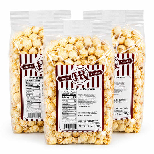 Three clear plastic bags of Poppin' Pops Butter Rum Popcorn arranged in a triangular stack on a white background, with the center bag fully visible and the side bags partially behind it.
