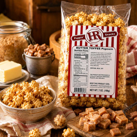 A bag of Poppin' IR Snacks Butter Toffee Popcorn is displayed on a rustic wooden table with bowls of caramel, butter, and loose popcorn pieces. The packaging features a red and white striped label with the brand logo 'Poppin' IR'.