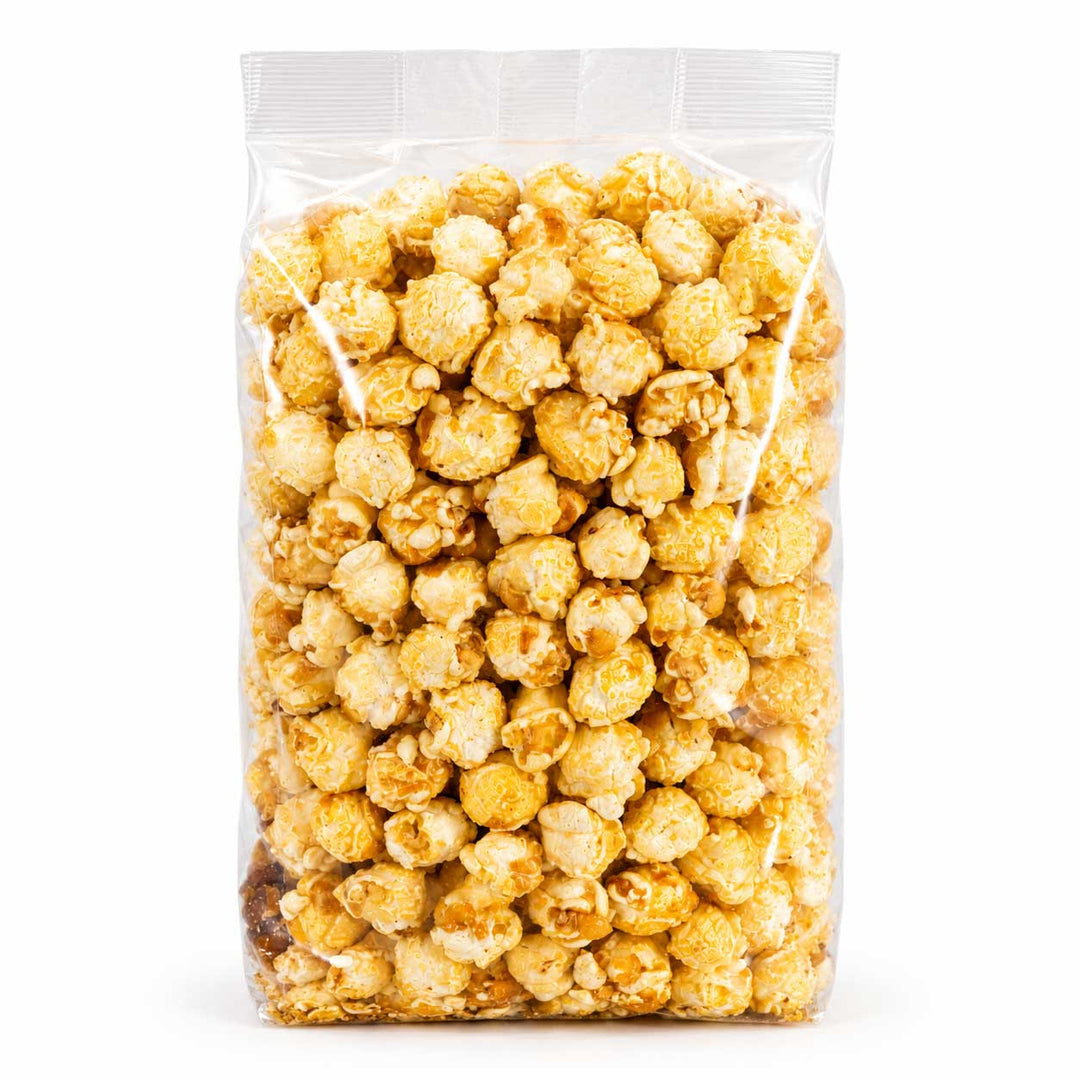 A clear plastic bag filled with caramel popcorn on a plain white background.