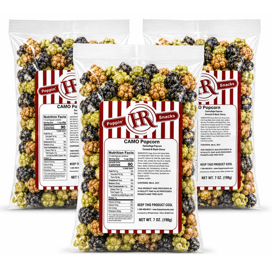 Three clear plastic bags of Poppin' Brunches CAMO Popcorn arranged in a fan shape on a white background. The bags contain a mix of red, black, and green popcorn kernels, and each bag has a white label with red and black branding.