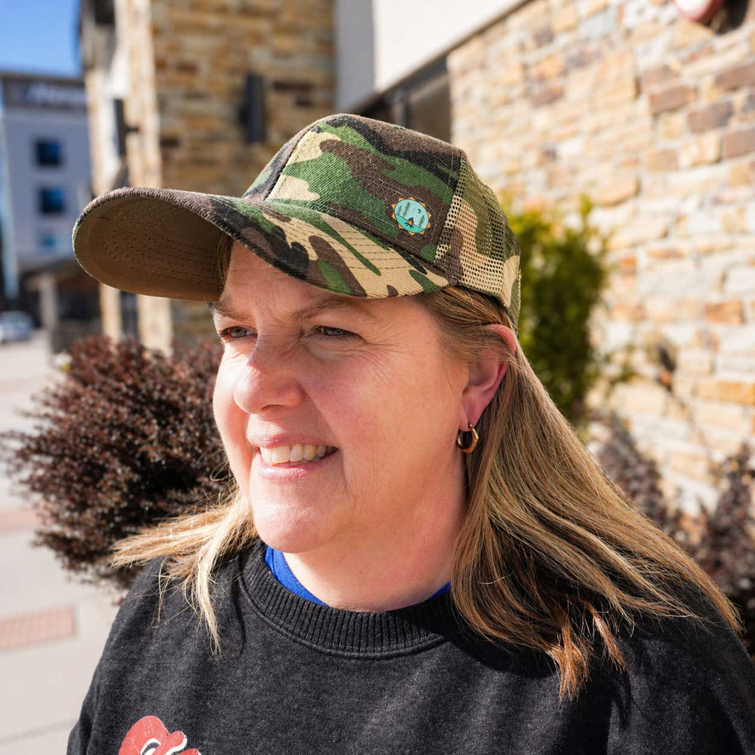 Person wearing a camouflage baseball cap outdoors with a stone building in the background