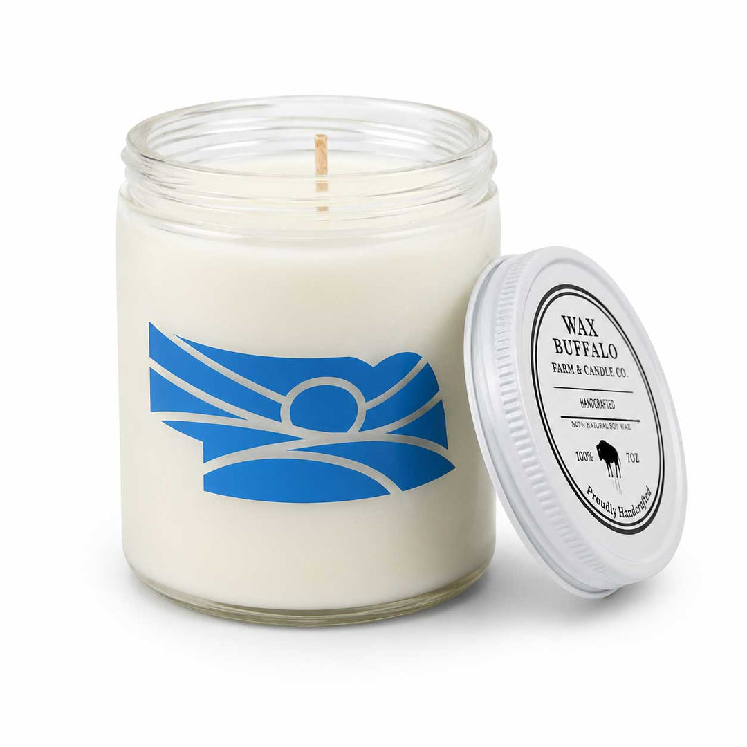 A white wax candle in a clear glass jar with a blue and white buffalo graphic on the front, shown with its white screw-on lid leaning against the jar on a white background.