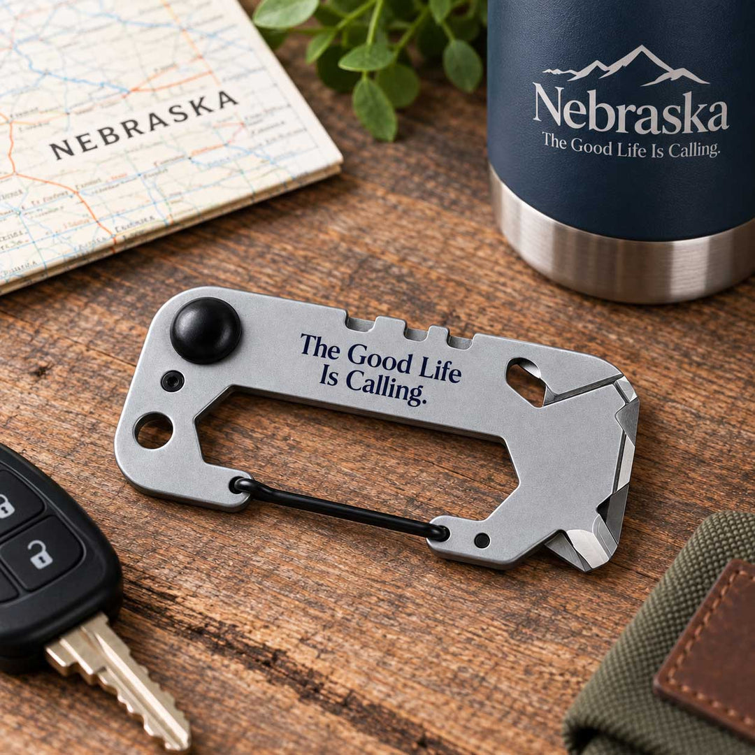 A silver multi-tool car keychain with the engraved text 'The Good Life Is Calling.' lies on a wooden tabletop.