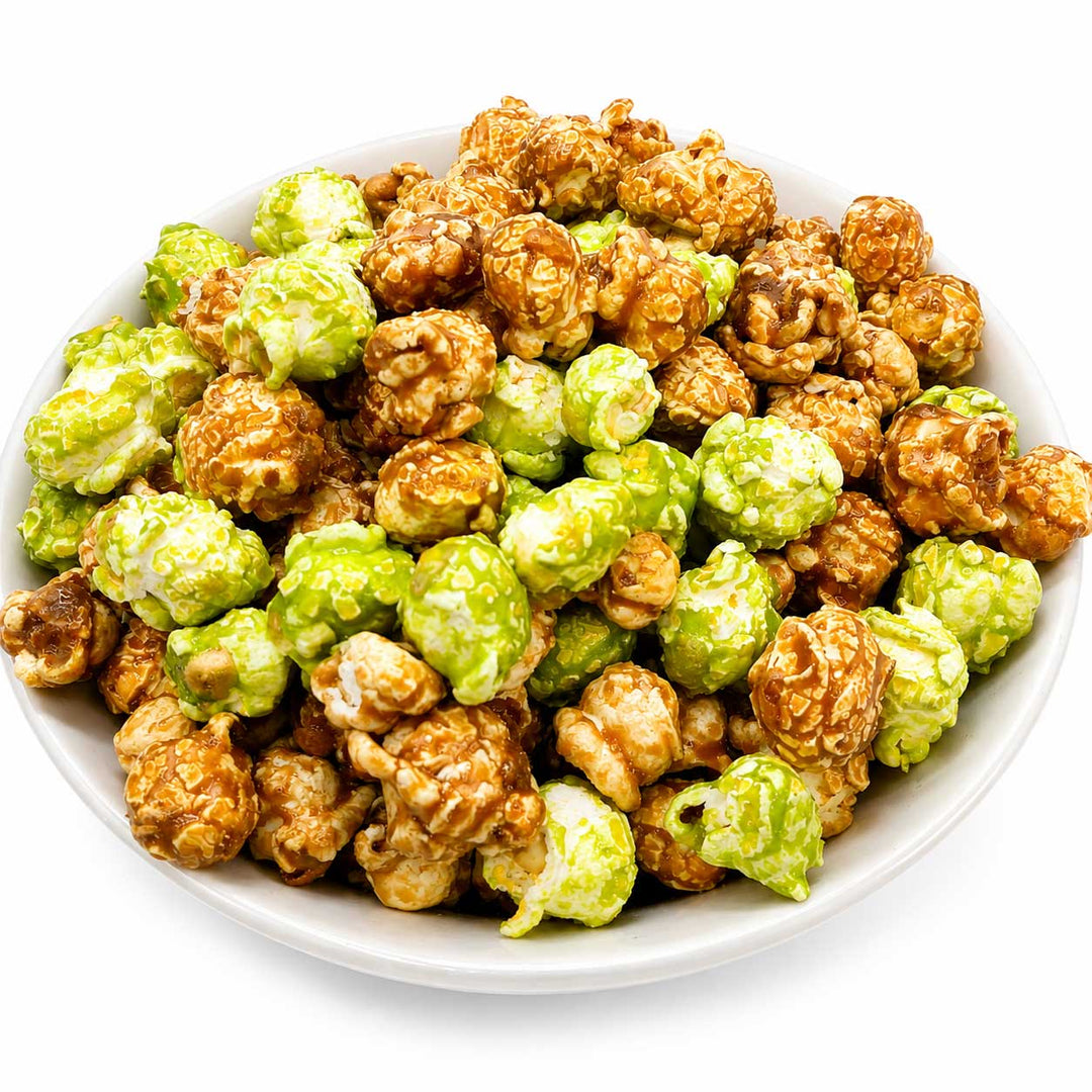A white bowl filled with mixed caramel popcorn, including some green-topped popcorn and brown caramel-coated kernels, on a white background.