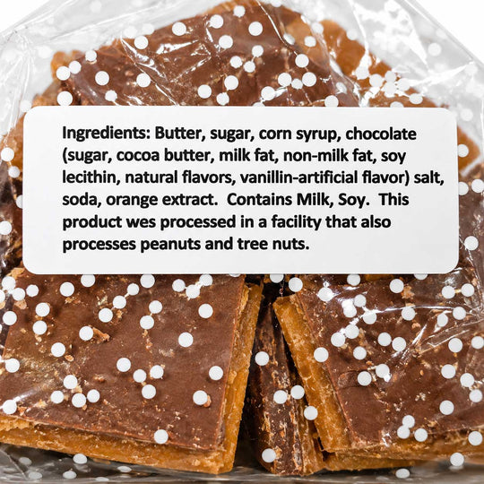 Chocolate-covered square candies or fudge pieces wrapped in clear plastic, with a white label showing ingredients and a nut allergy warning.