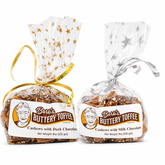 Two packaged bags of Berli's Buttery Toffee Cashews on a white background. The left bag has gold stars on the wrapper and a gold ribbon, while the right bag has silver stars on the wrapper and a silver ribbon.