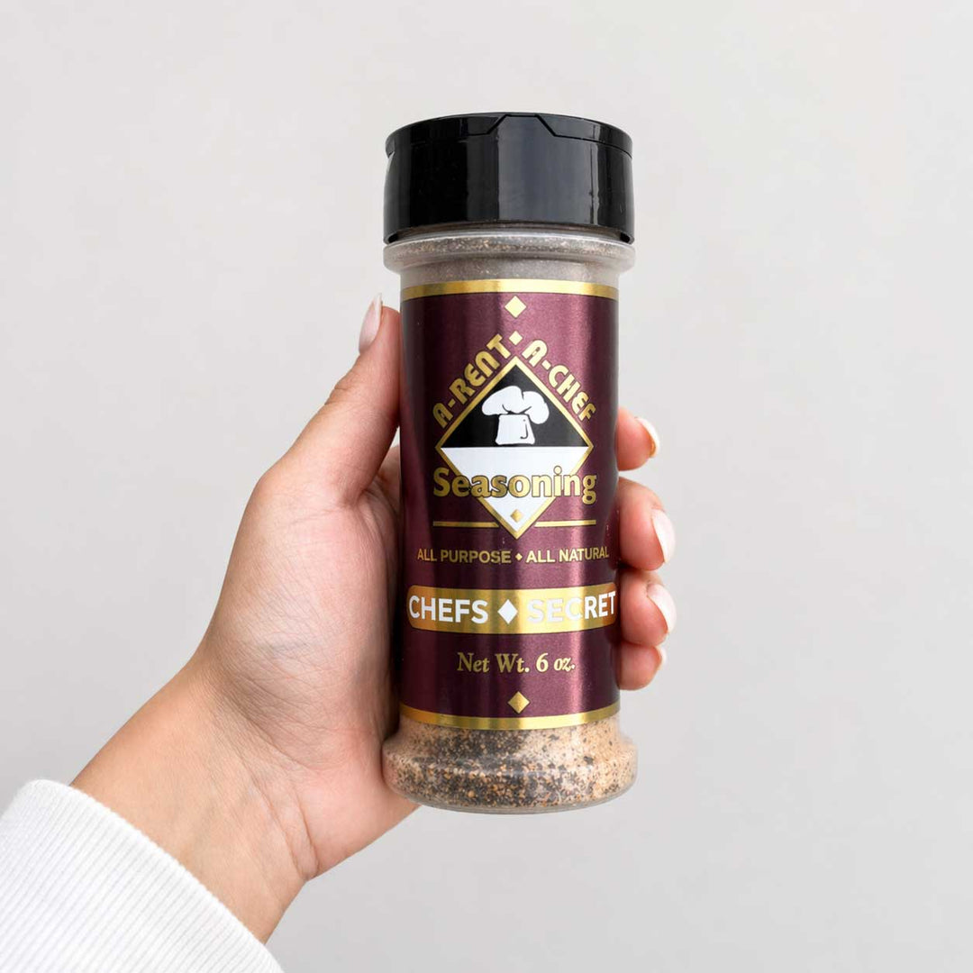 Hand holding a jar of 'A-Rent-A-Chef' seasoning against a plain background