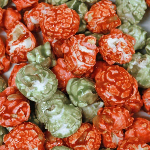 A close-up pile of popcorn coated in orange and light green candy, with some pieces showing white candy highlights.