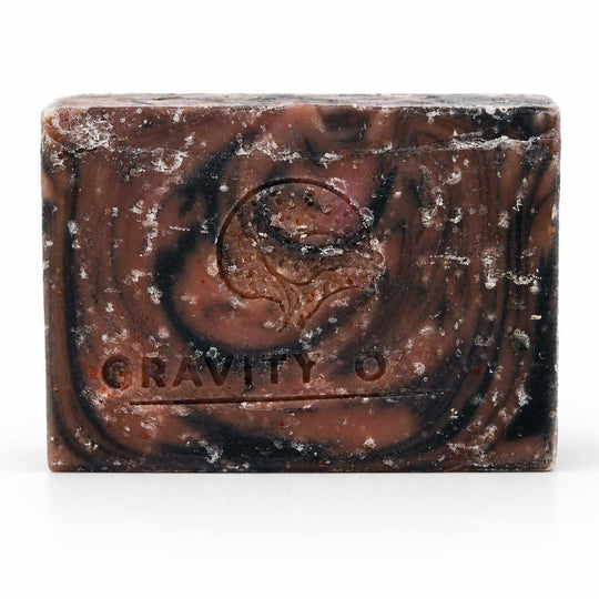 A rectangular bar of marbled dark brown and black soap with white crystalline specks, embossed with a swirl design and the brand name 'GRAVITY O'.