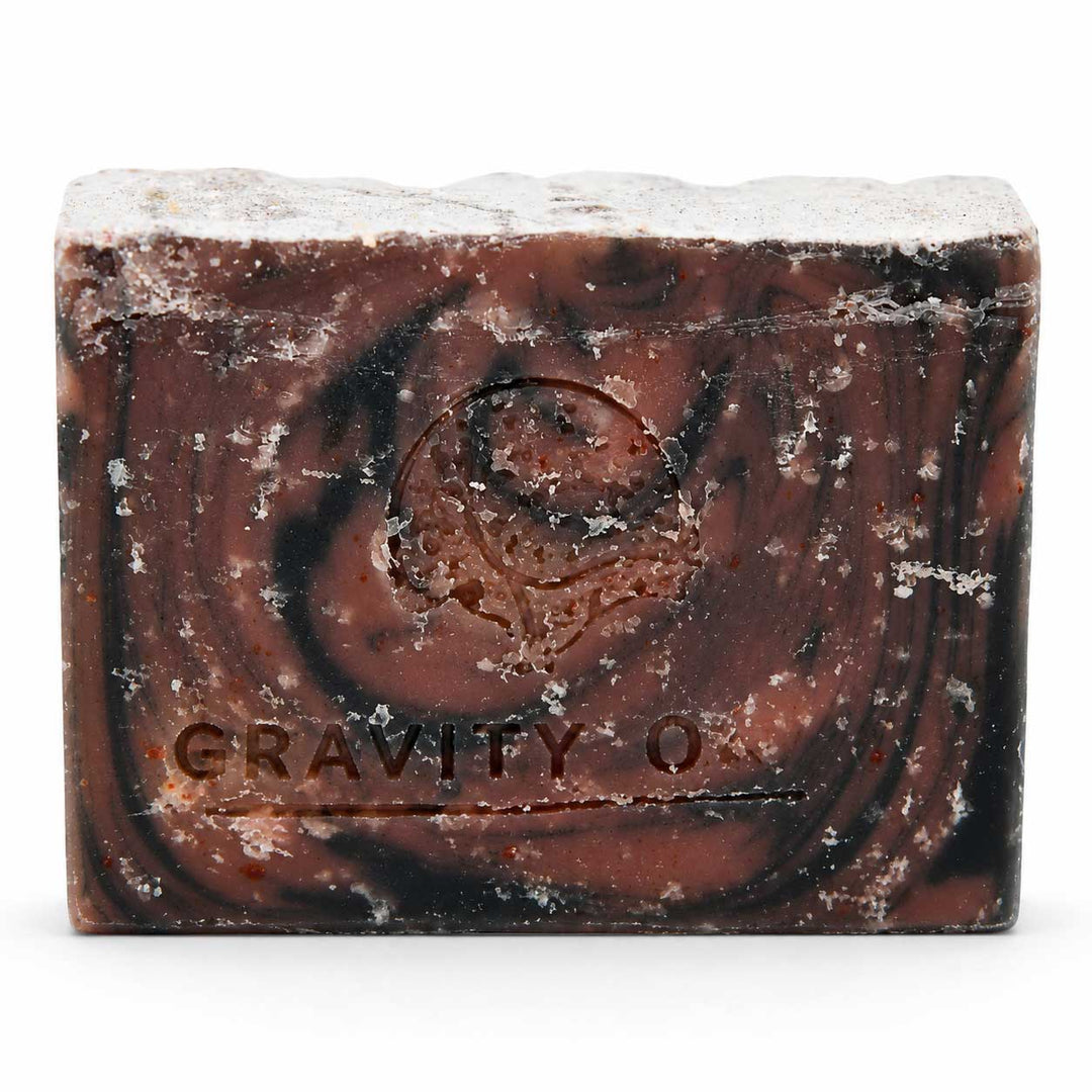 A rectangular bar of textured soap with a dark brown and black swirled pattern and white crystalline specks, embossed with the brand name 'GRAVITY O'.