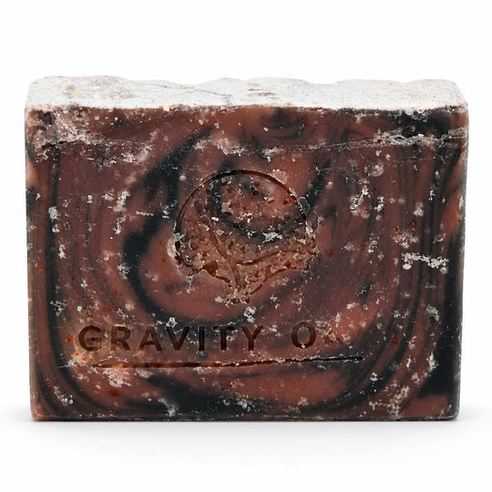 A rectangular bar of textured soap with a dark brown and black swirled pattern and white crystalline specks, embossed with the brand name 'GRAVITY O'.