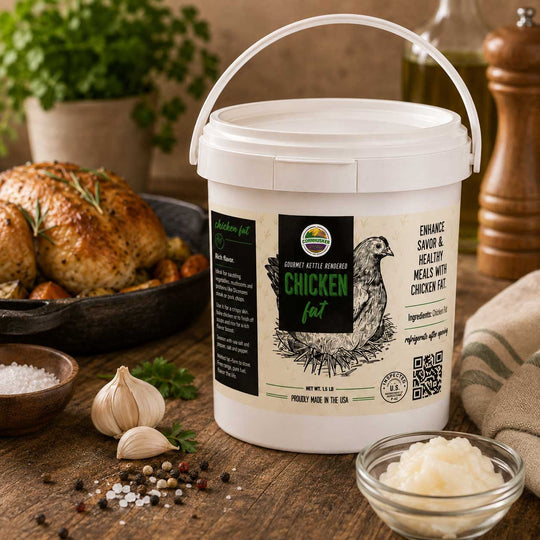 A white plastic tub of Cornhusker Kitchen Chicken Fat with a white handle, set on a rustic wooden table surrounded by cooking ingredients and a roasted chicken.