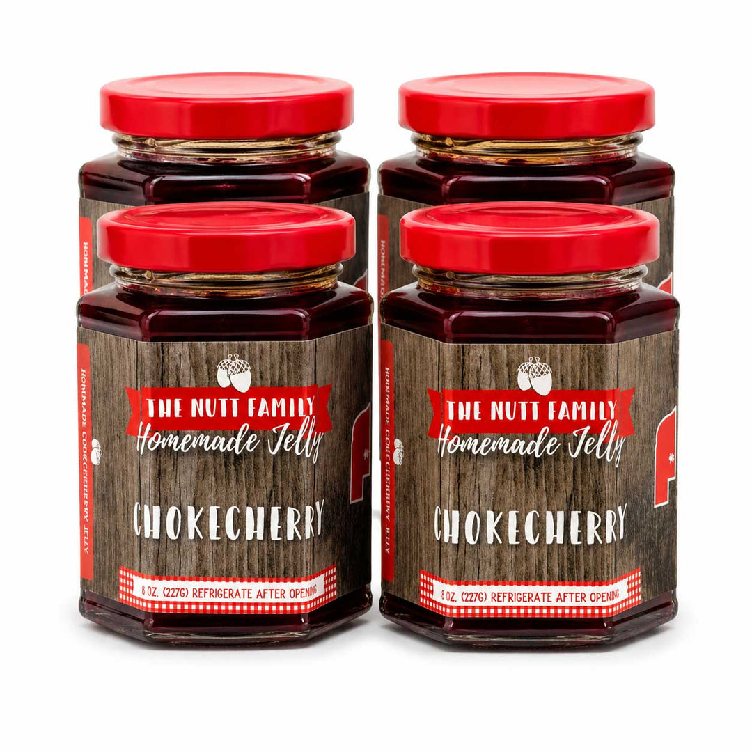 Four jars of The Nutt Family Homemade Chokecherry Jelly with red lids on a white background.